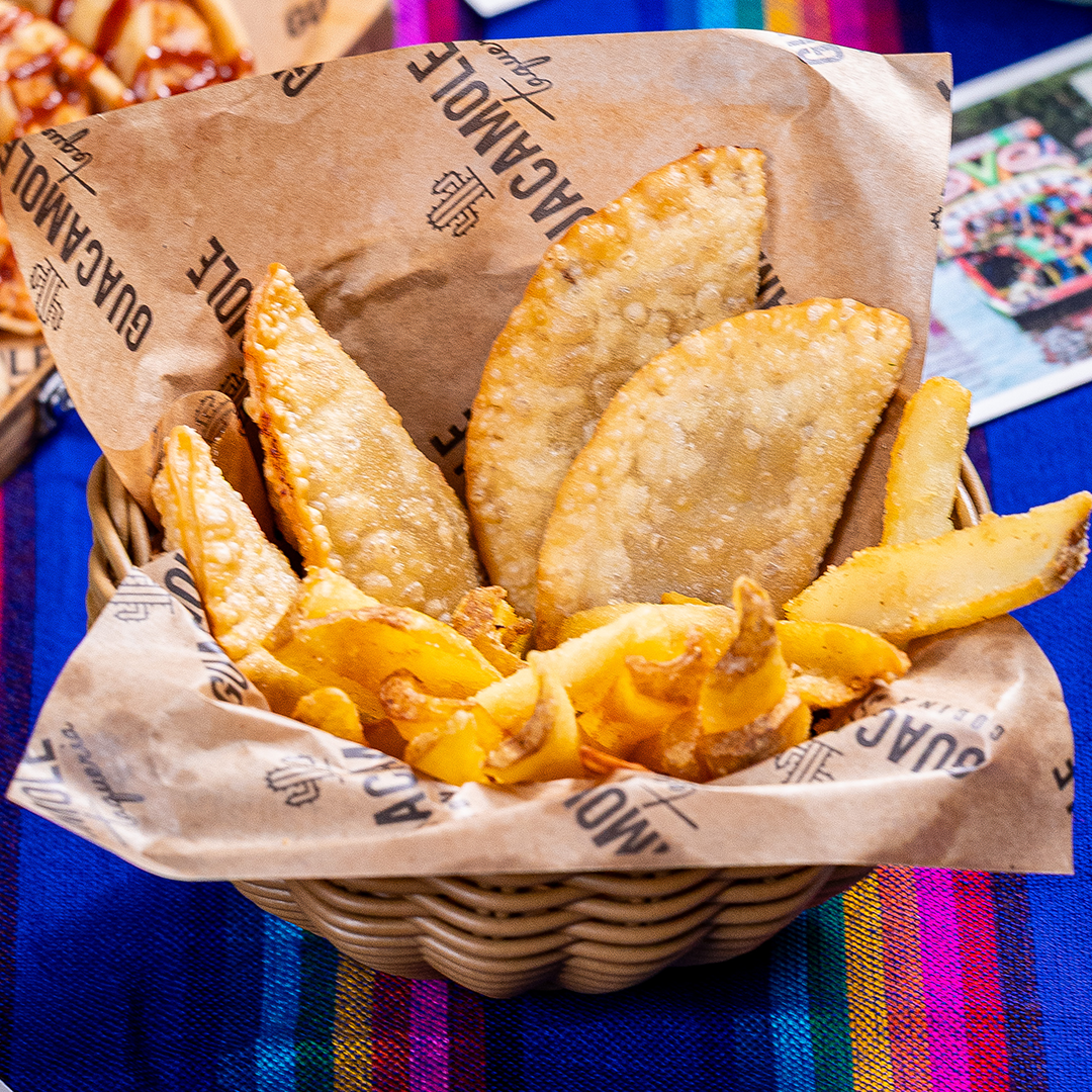 Cesta de empanadas fritas com batatas fritas douradas sobre uma toalha de mesa listrada e colorida.