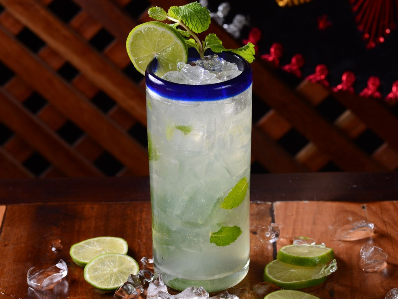 Bebida alta estilo mojito com rodelas de limão e hortelã sobre uma mesa de madeira.