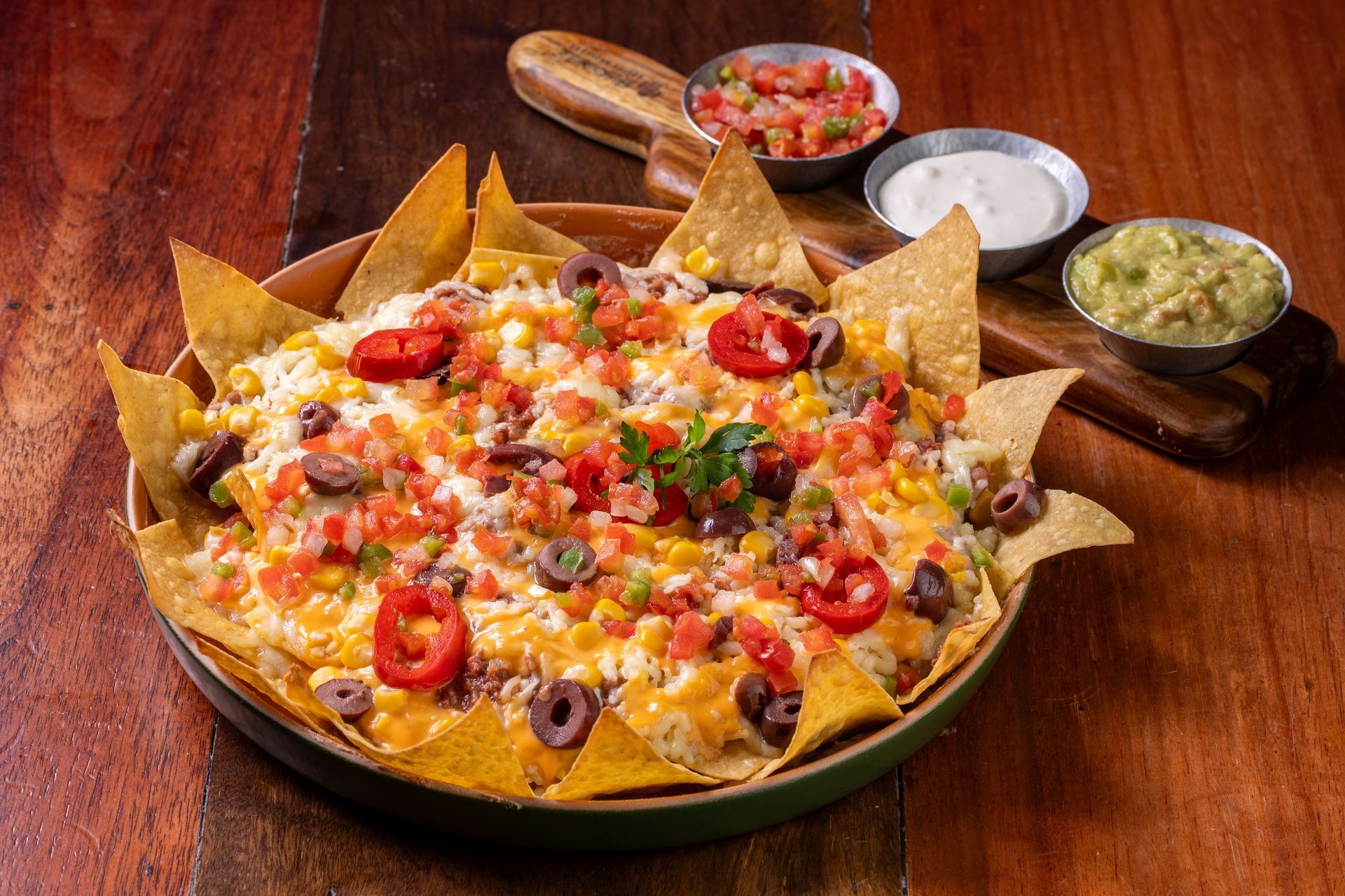 Nachos recheados com tomates, azeitonas, cebolas e queijo, servidos com salsa, guacamole e creme azedo.