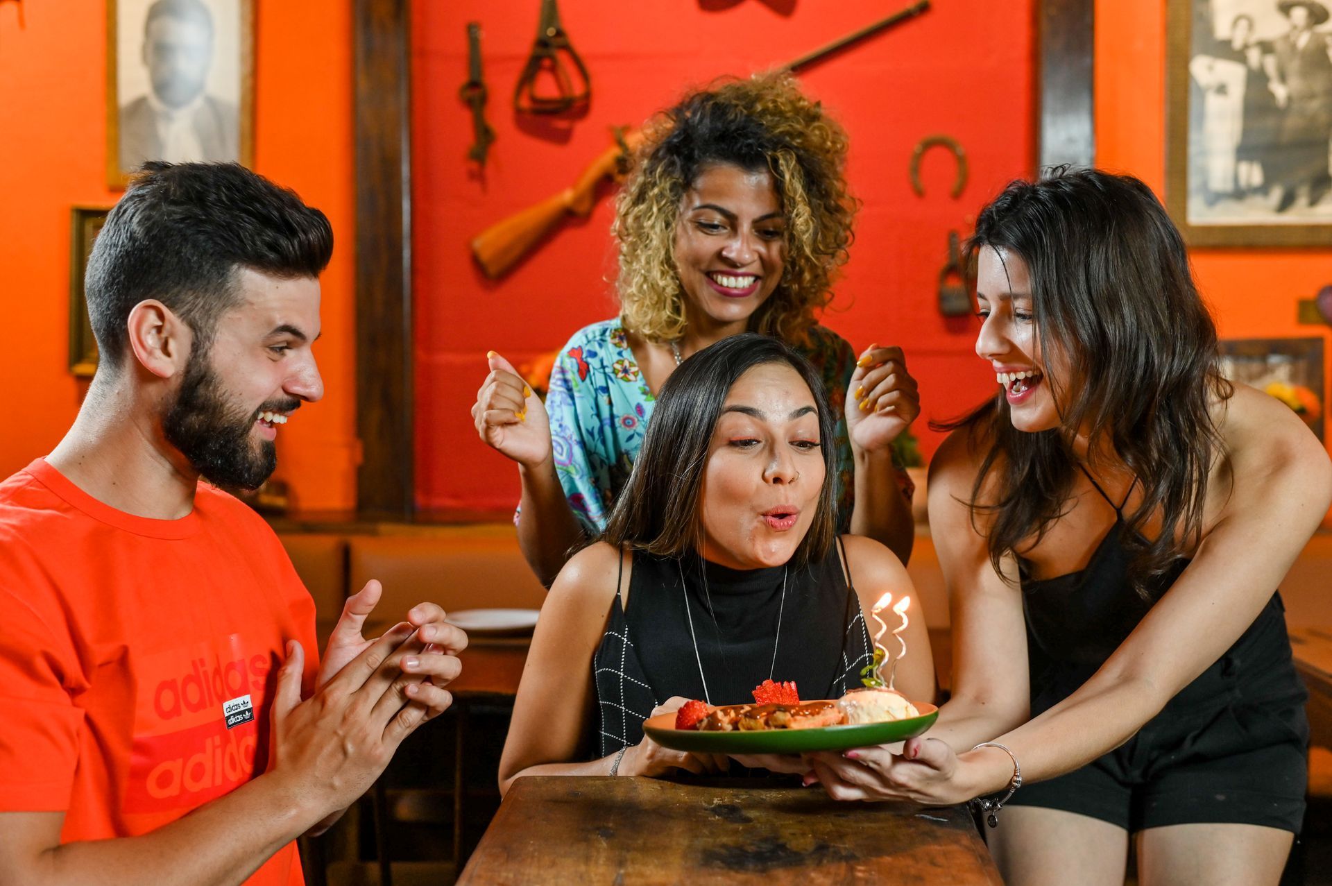 Amigos comemorando com um bolo de aniversário em um restaurante aconchegante com luz alaranjada.