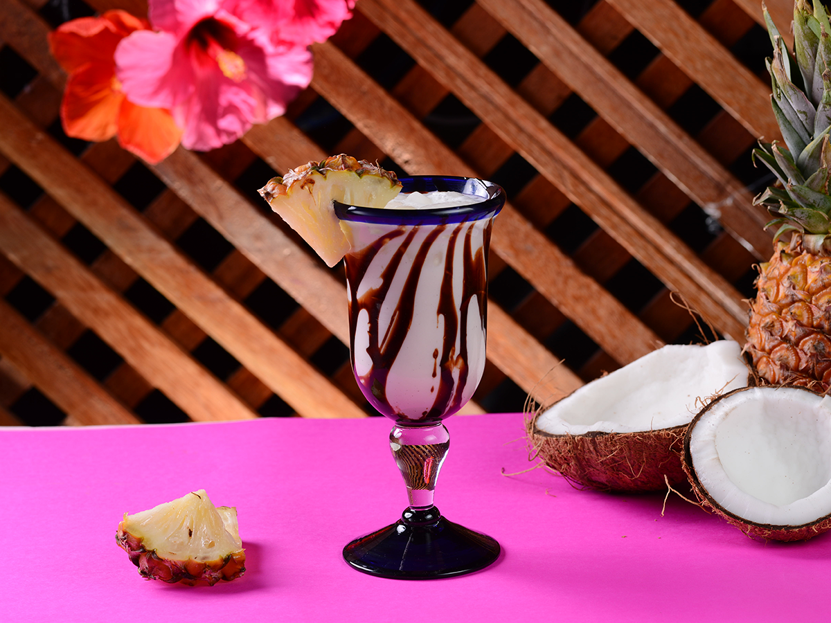 Sobremesa de chocolate servida em taça com metades de coco sobre uma superfície rosa e fundo de treliça de madeira.