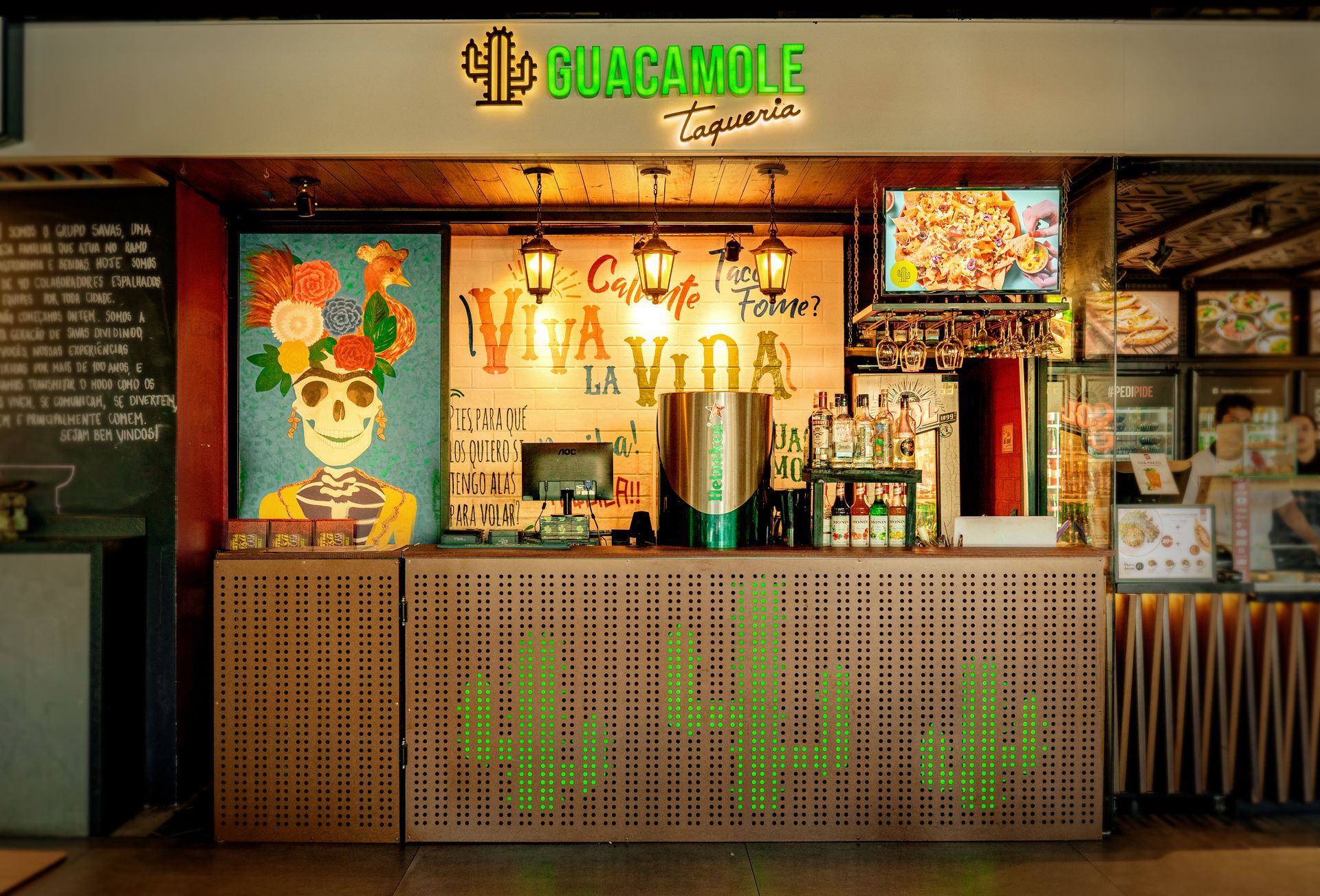 Balcão de restaurante de guacamole com cardápios, placas coloridas e painel frontal com tema de cactos.