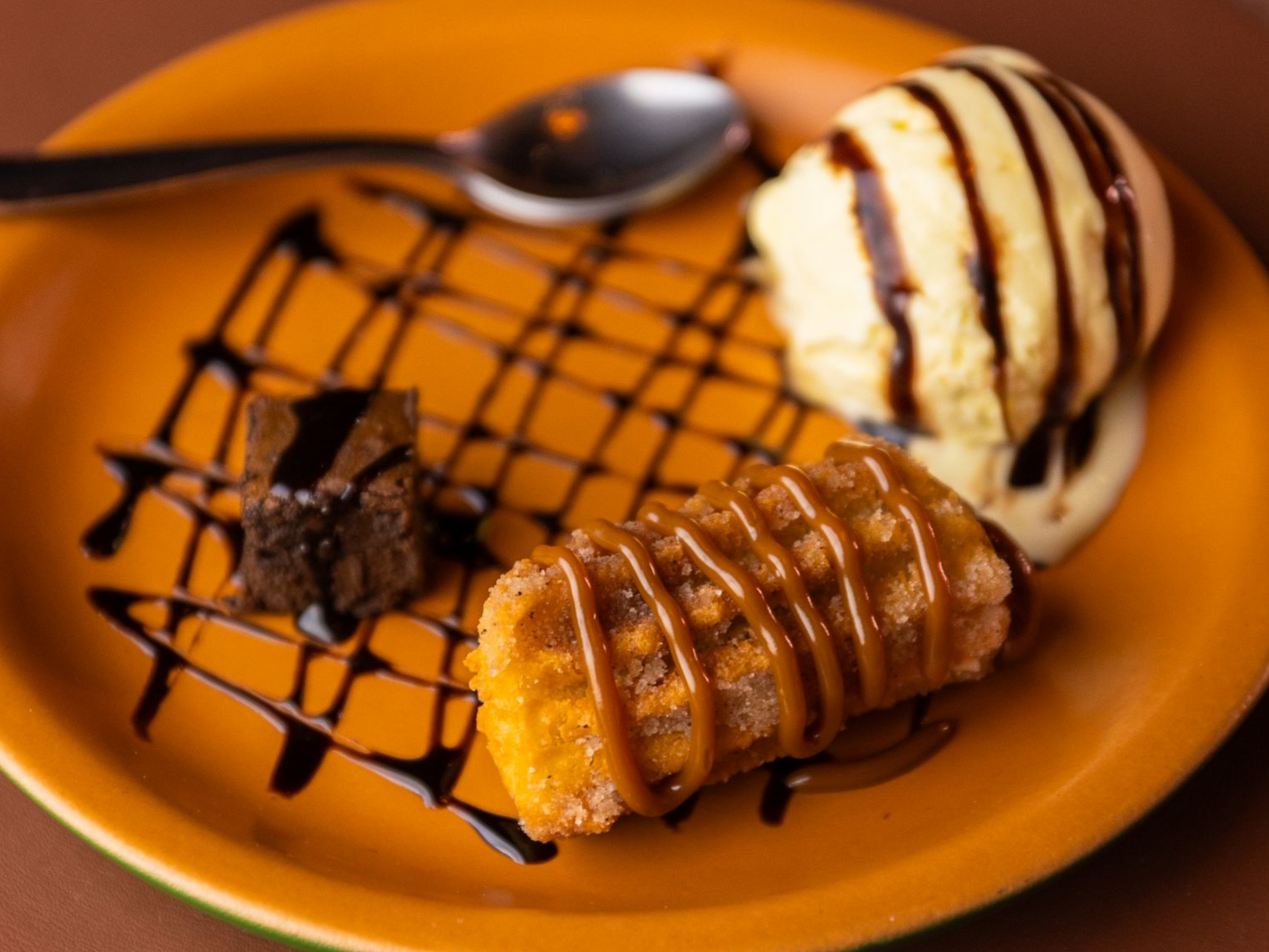 Prato de sobremesa laranja com massa folhada decorada com calda de chocolate e uma bola de sorvete de baunilha com molho.