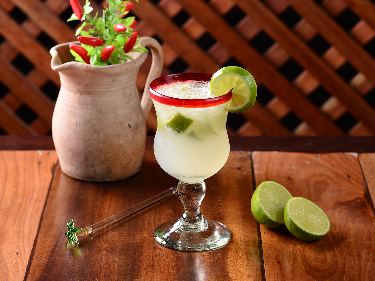 Margarita com limão sobre uma mesa de madeira ao lado de uma jarra de barro com morangos.