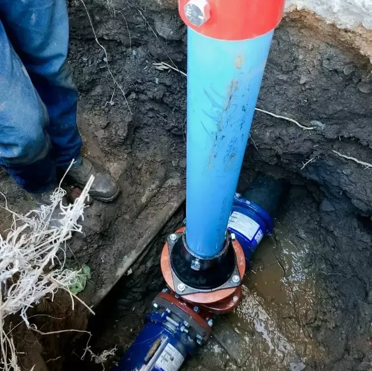 A man is standing next to a blue pipe in the dirt