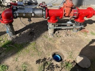 A red fire hydrant is sitting in the dirt next to a blue pipe.