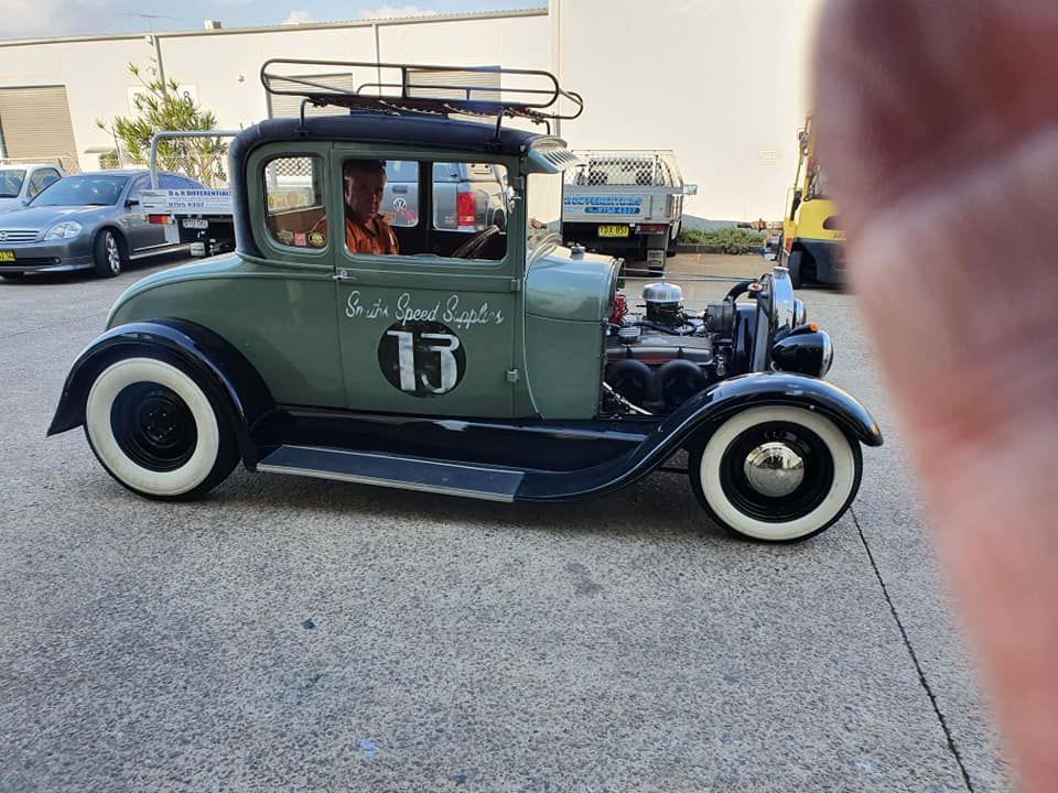 Vintage green-and-black hot rod parked outdoors, with whitewall tires and roof rack