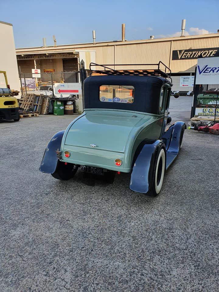 Customized vintage hot rod with blue and mint paint parked on gravel outside a shop