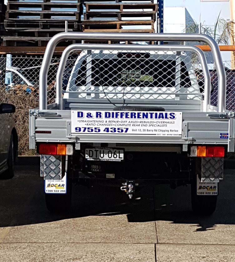 Silver flatbed truck with D&R Differentials sign and chain-link rear gate, parked outdoors