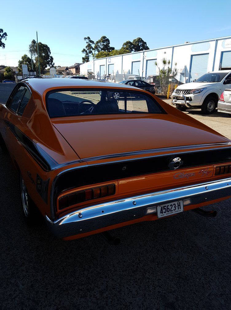 Rear view of a brown classic muscle car parked on a street beside buildings and other cars.