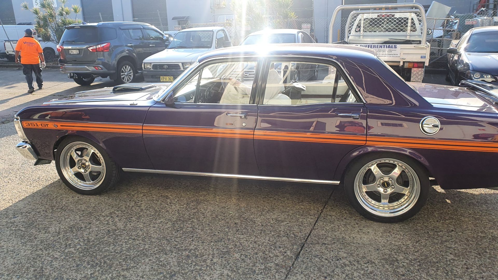 Purple classic coupe with orange stripe, parked outdoors on a sunlit street.