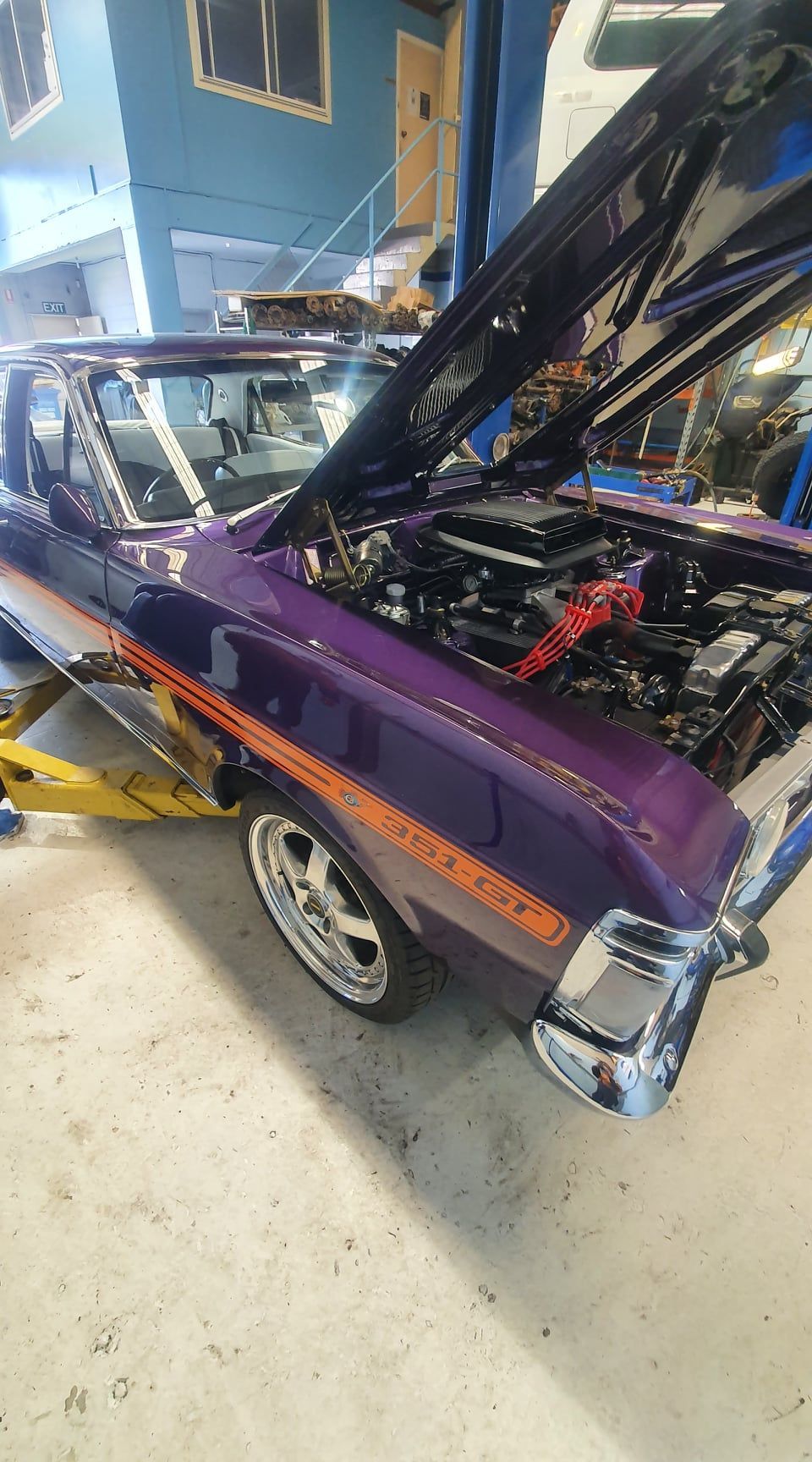 Purple classic car with hood open, shown in a garage, with chrome details and a front wheel visible