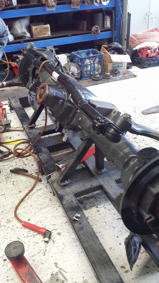 Disassembled vehicle drivetrain on a workbench in a garage, with tools and parts scattered around.