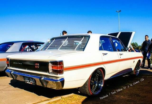 Classic white muscle car with orange stripes parked outdoors under a clear blue sky.