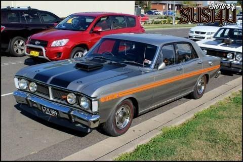 Classic silver-and-black muscle car parked on a street, with other vehicles in the background.