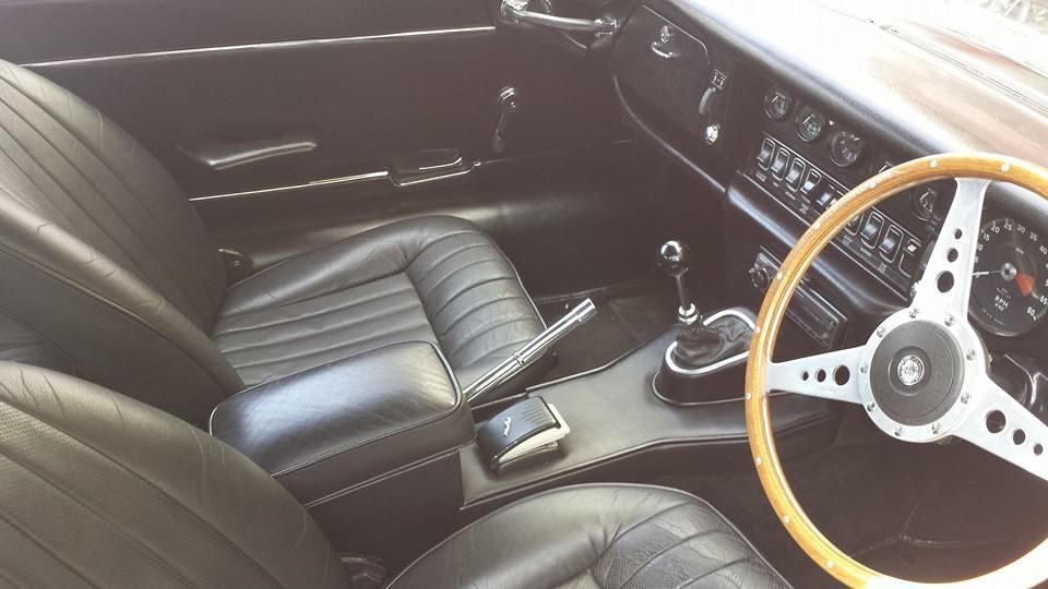 Classic car interior with black leather seats, wood-rim steering wheel, and manual gear shift