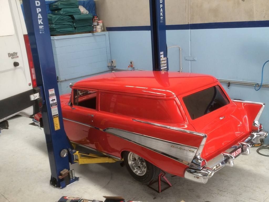 Red classic car on a lift in an auto shop, with a chrome rear and open trunk area.