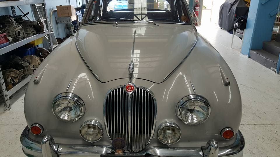 Front view of a classic beige vintage car in a garage, with round headlights and a chrome grille
