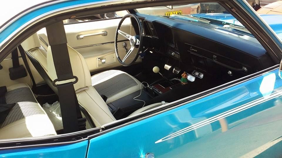 Interior of a turquoise classic convertible with white seats and a black dashboard, viewed from above