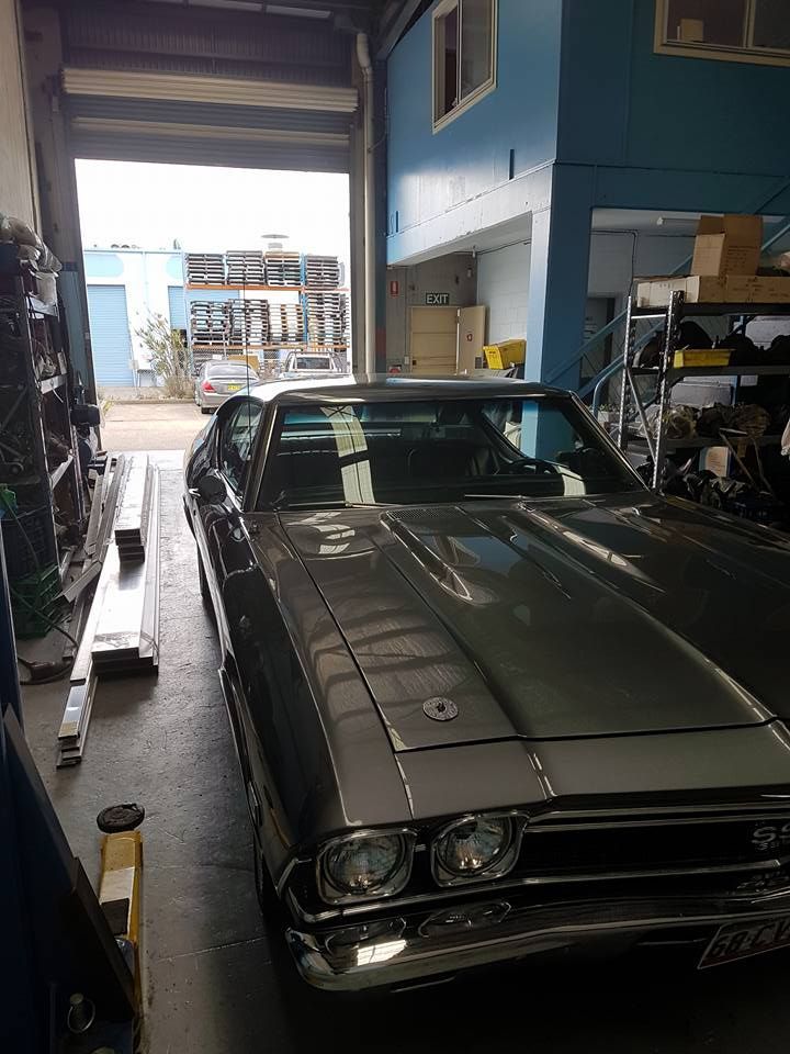 Classic dark green car inside a garage, viewed from the front near an open doorway.