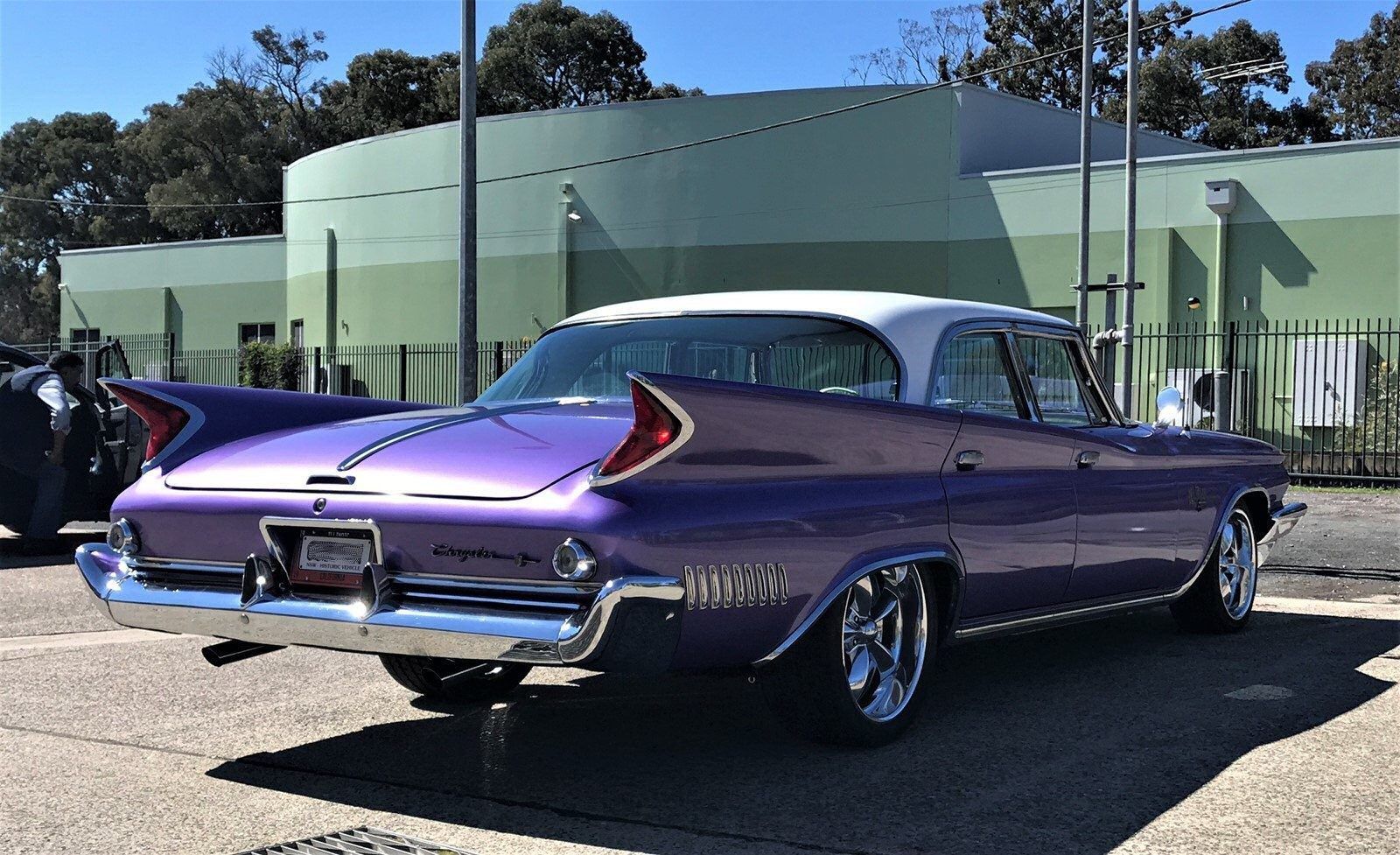Purple classic car parked outside a green building on a sunny day