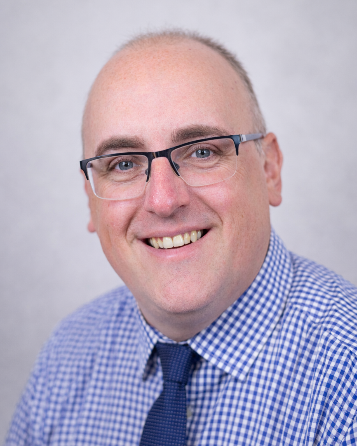 Smiling man in glasses and blue checkered shirt against a light gray background