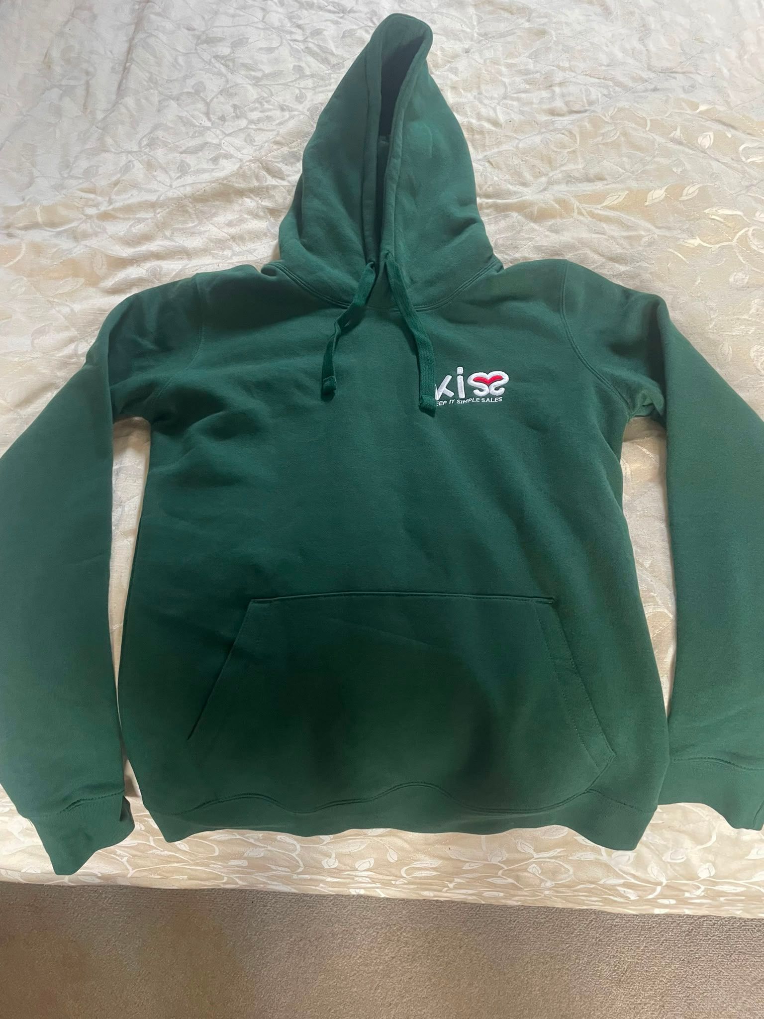 Green hooded sweatshirt with a small chest logo laid flat on a light textured surface