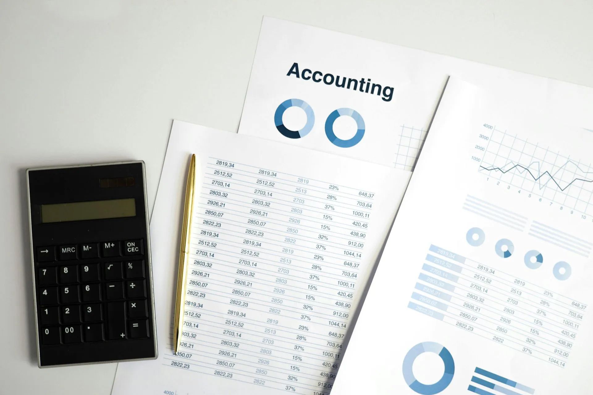 Calculator, pen, and accounting documents with charts and data on a white surface.