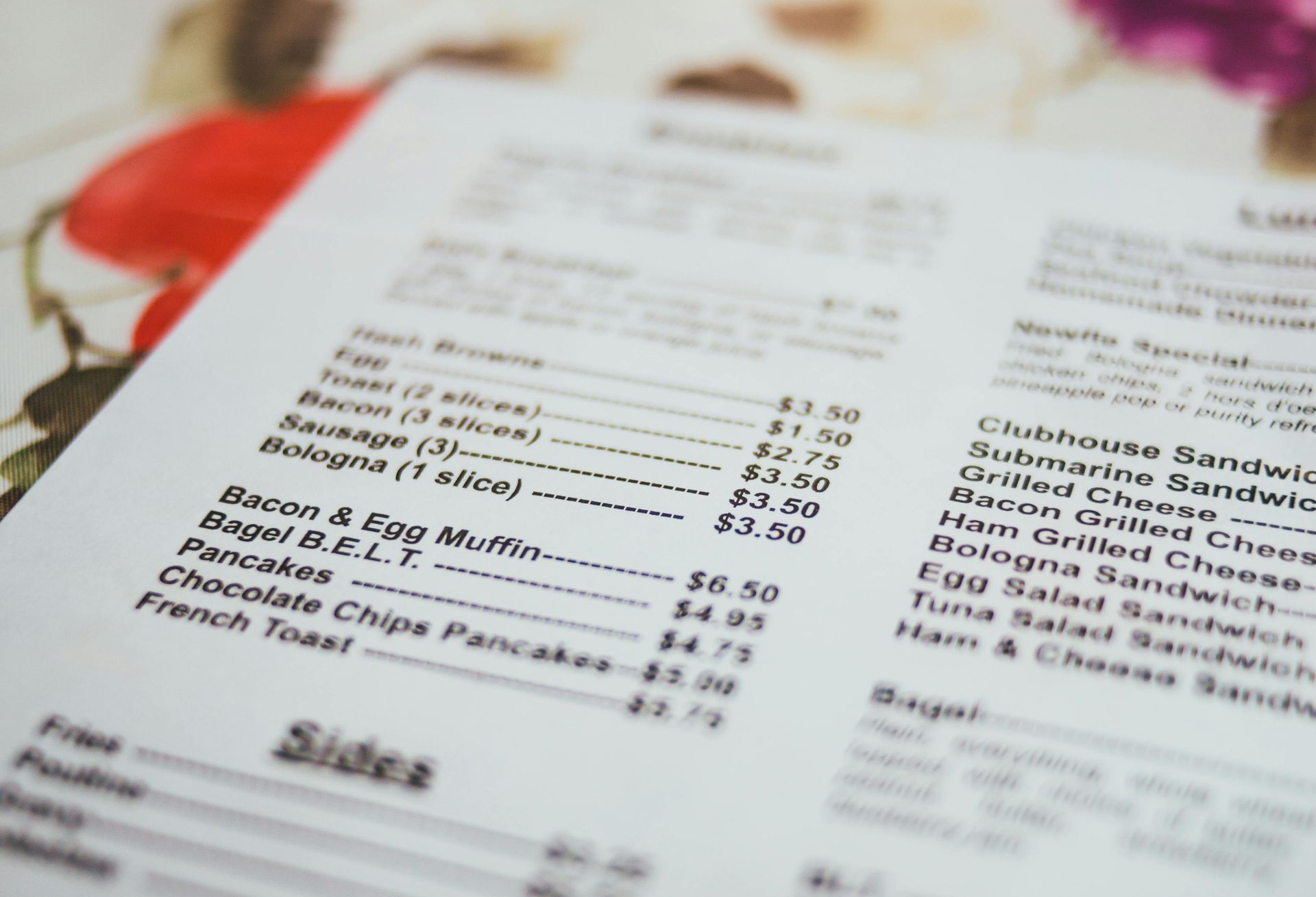 Close-up of an open menu on a floral tablecloth, with blurred pages and red accents.