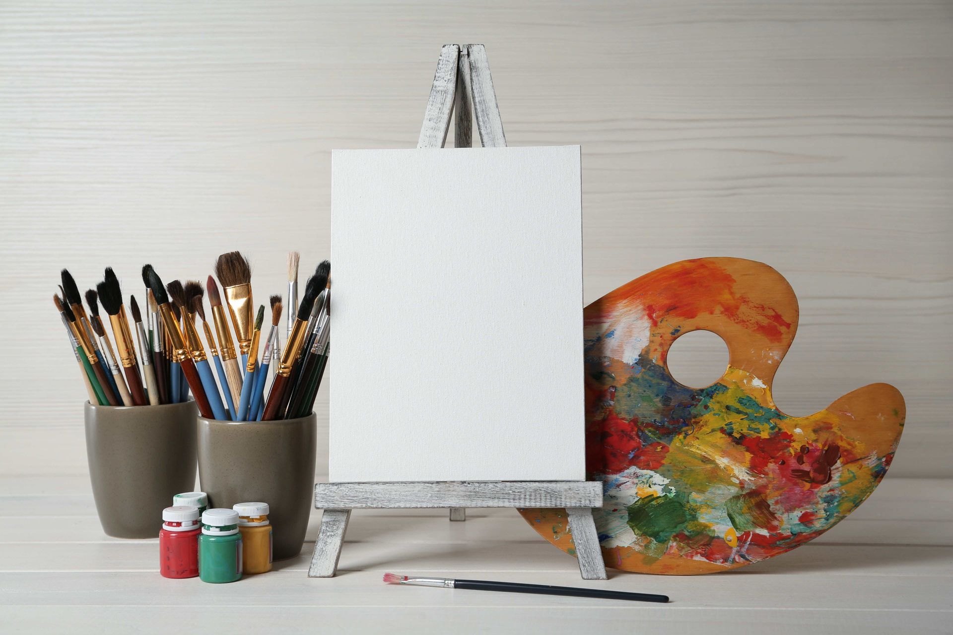 a palette with a hole in it sits next to an easel and brushes