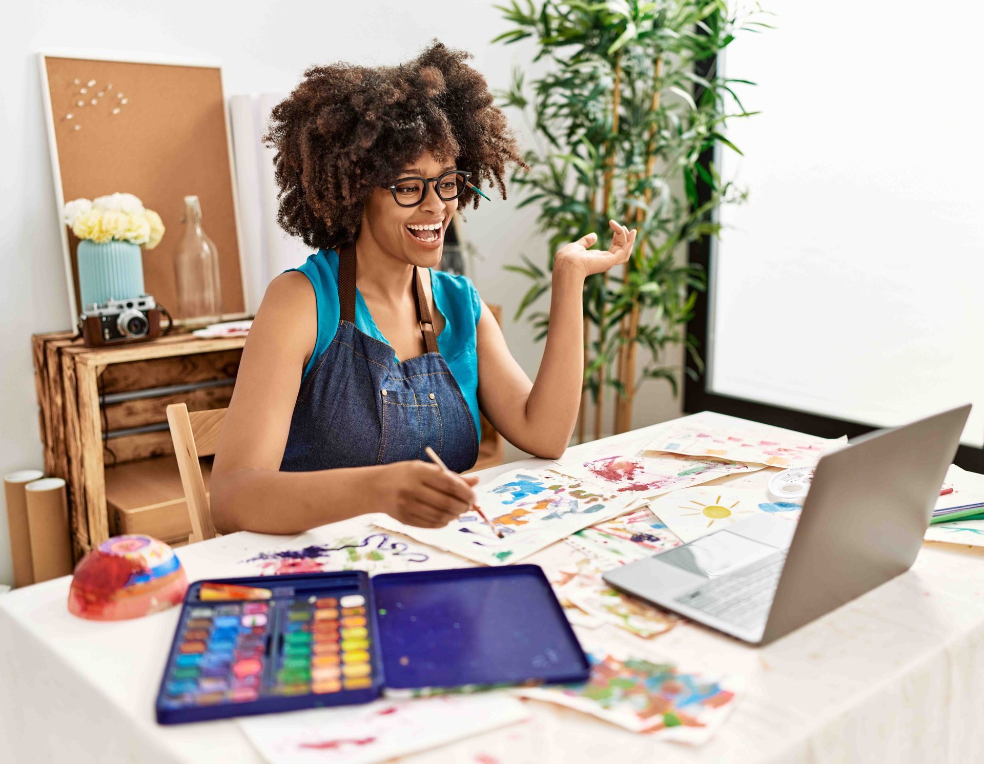 a woman is sitting at a table with a laptop and painting