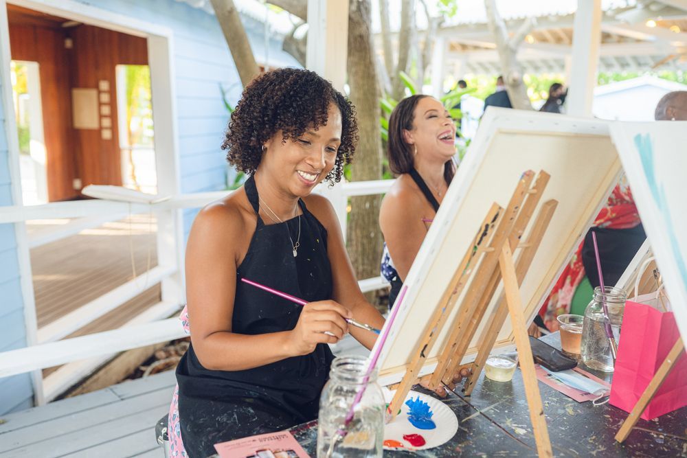 a group of people are sitting at tables painting flowers