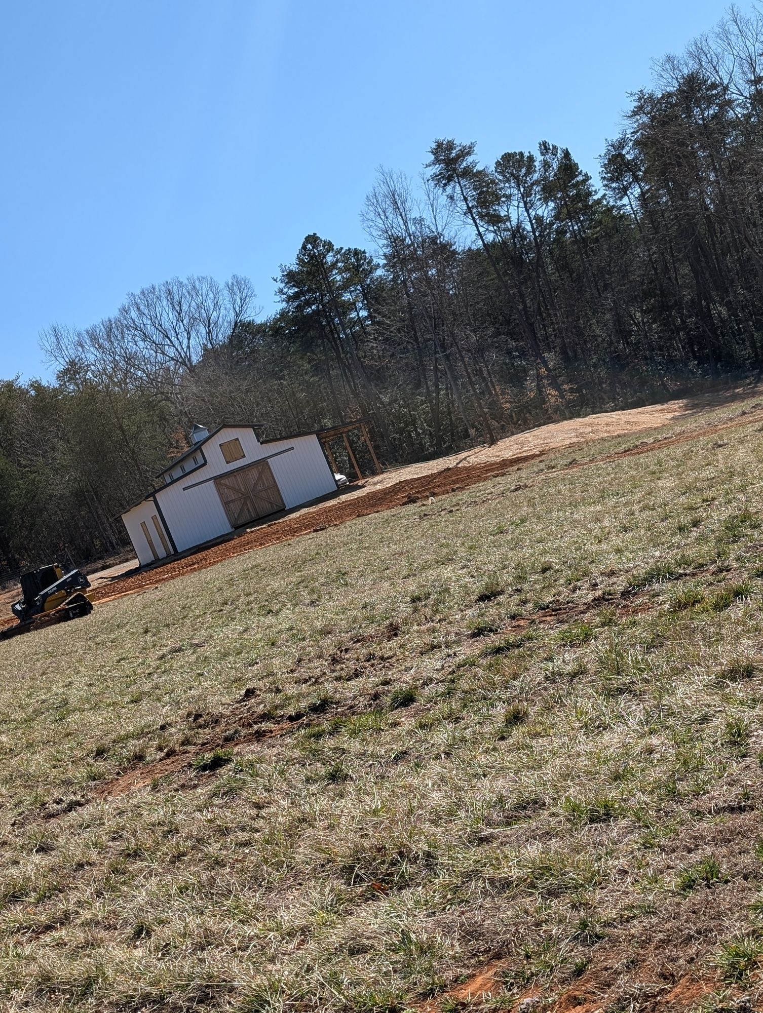 Tilted view of a grassy field with a small white shed and trees under a clear blue sky