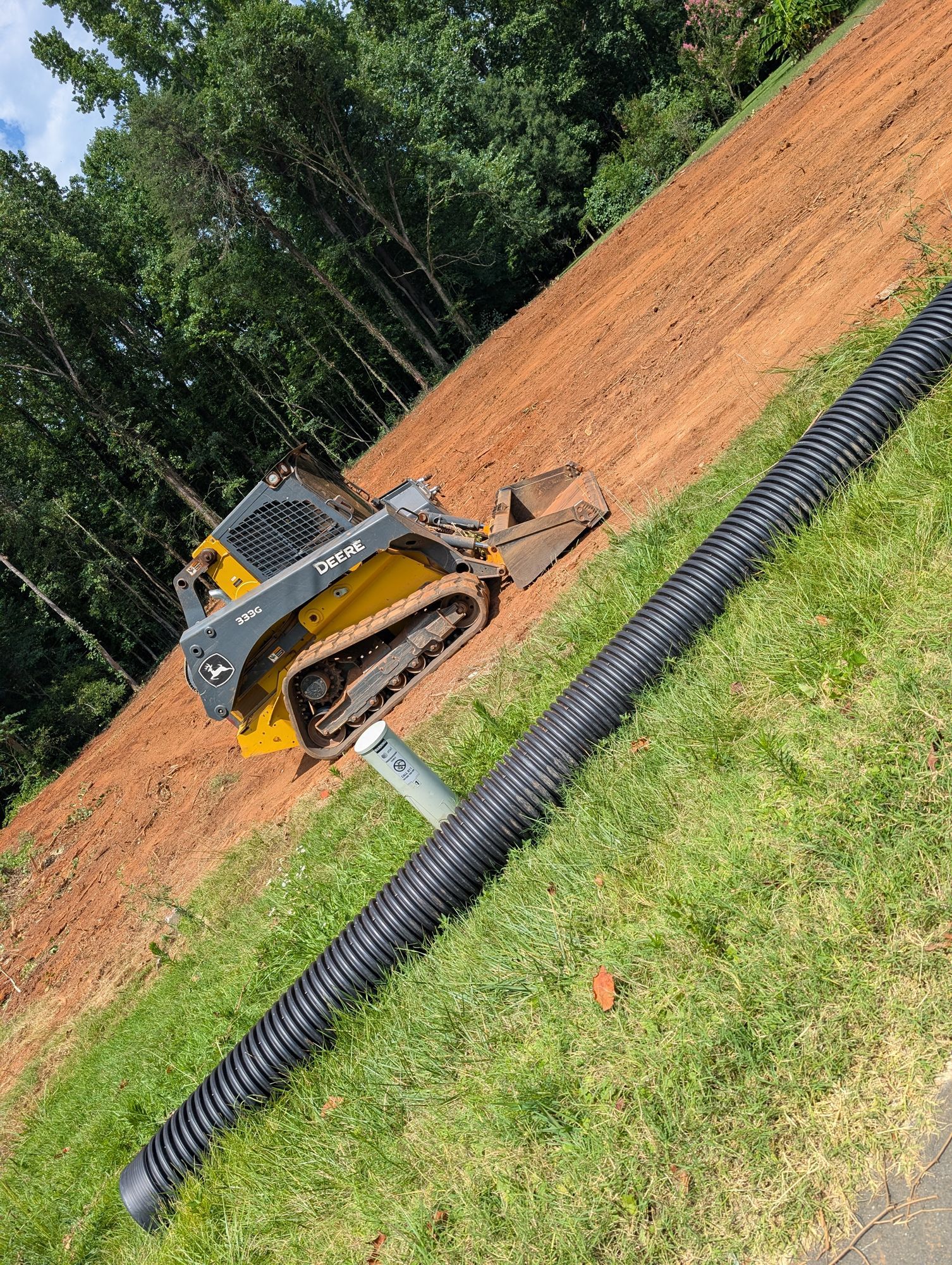 Yellow bulldozer beside black drainage pipe on a dirt construction site with trees in the background