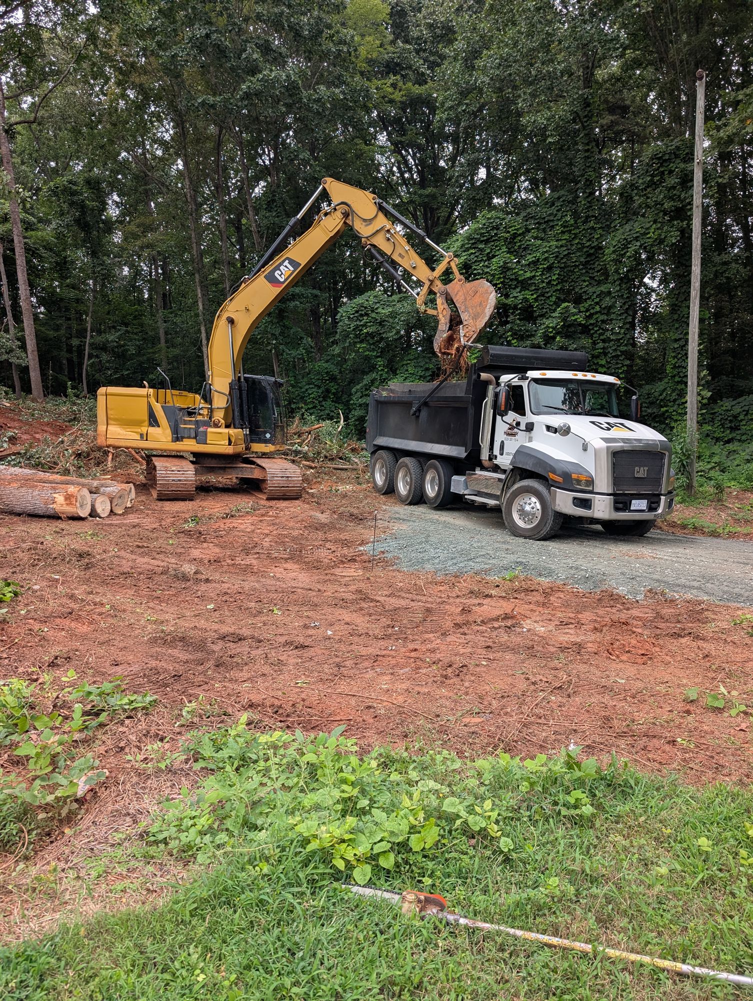 Excavator loading dirt into a dump truck at a wooded construction site