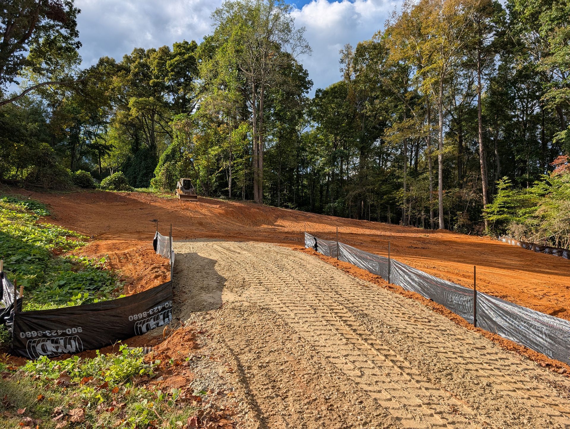 Gravel driveway under construction on a wooded hillside with fresh soil and erosion control netting