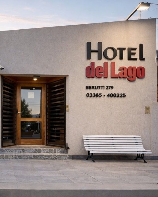 Un letrero del Hotel del Lago sobre una puerta, con un banco blanco frente a un edificio de color beige.