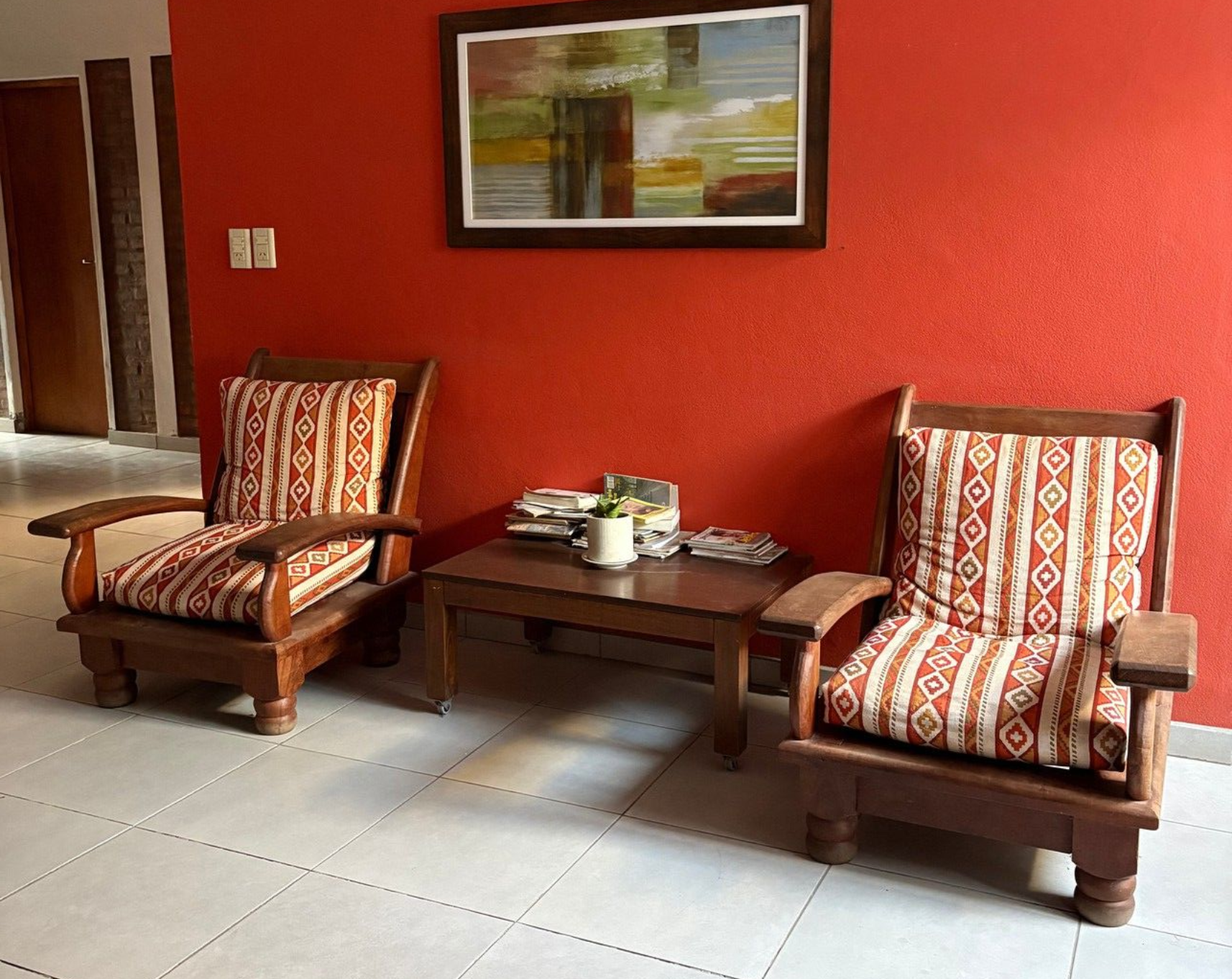 Patio con paredes rojas, dos tumbonas a rayas, una mesa baja de madera y cuadros enmarcados en la pared.