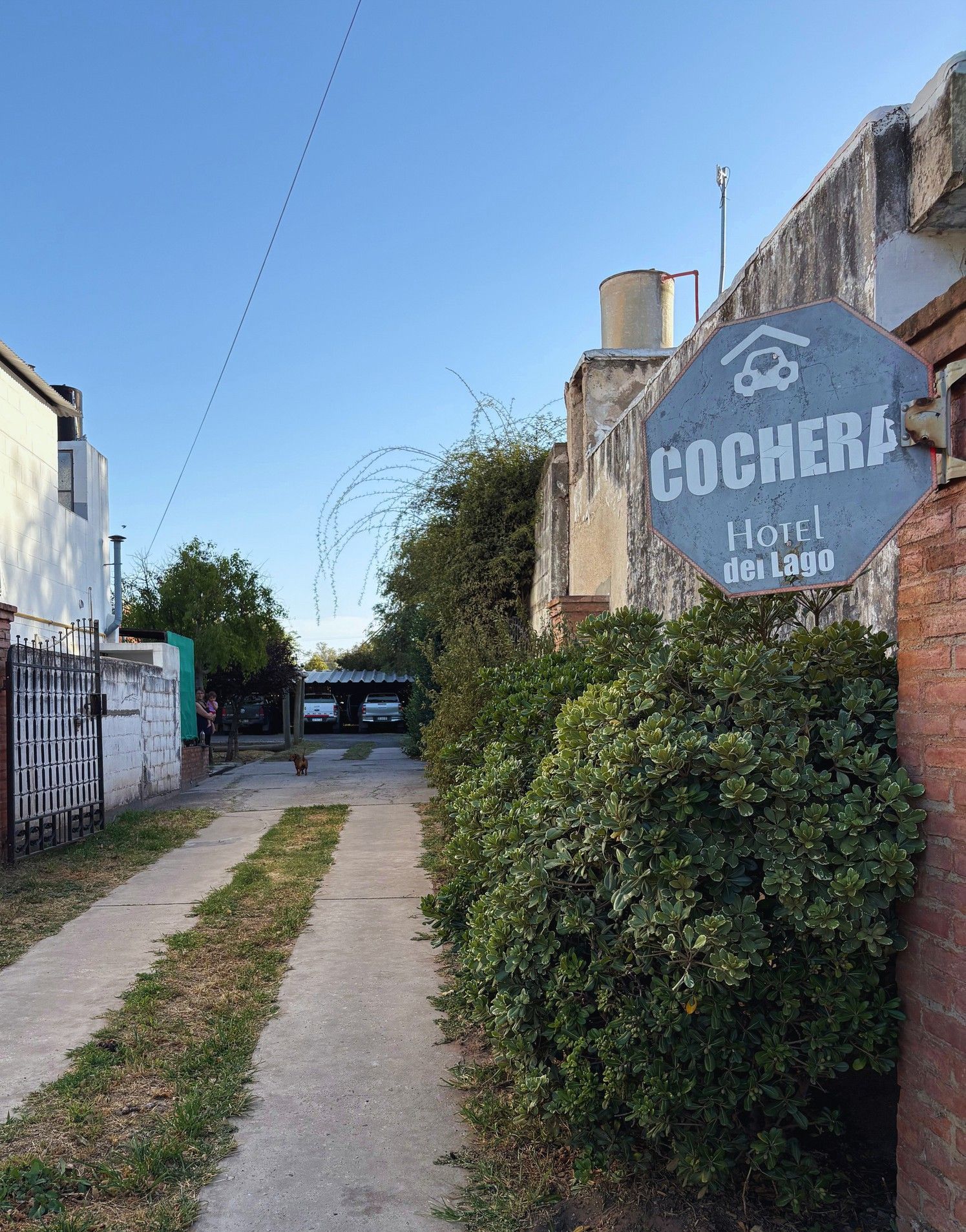 Callejón estrecho con camino de grava, arbustos y un letrero azul que dice 