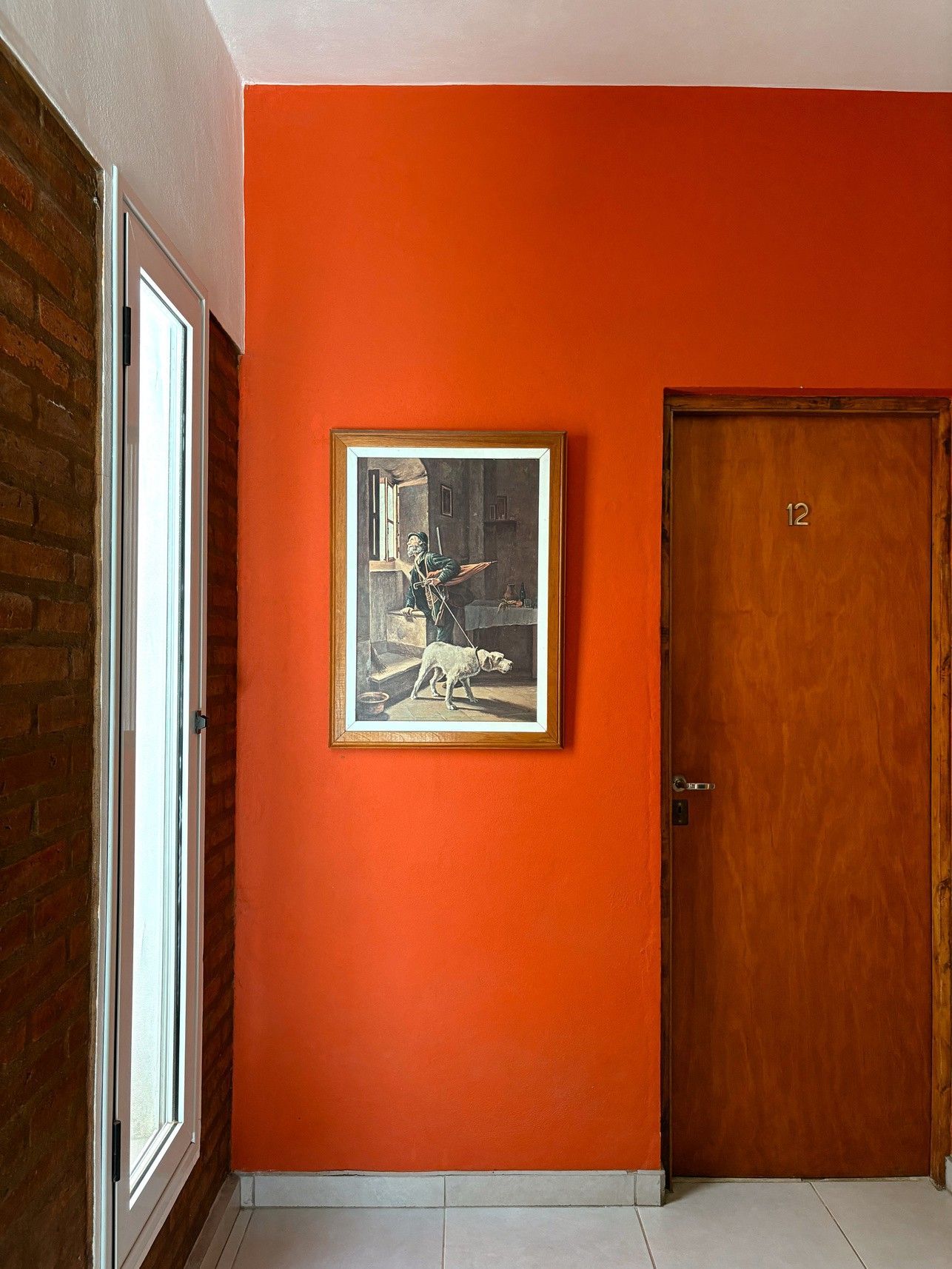 Pasillo naranja con un cuadro enmarcado y una puerta de madera a la derecha.