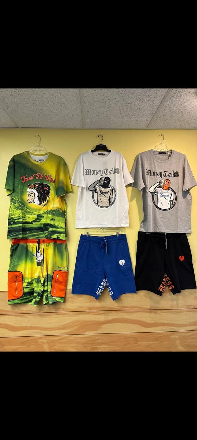 Three outfits hanging against a yellow wall, each featuring a graphic t-shirt paired with matching or coordinating shorts.