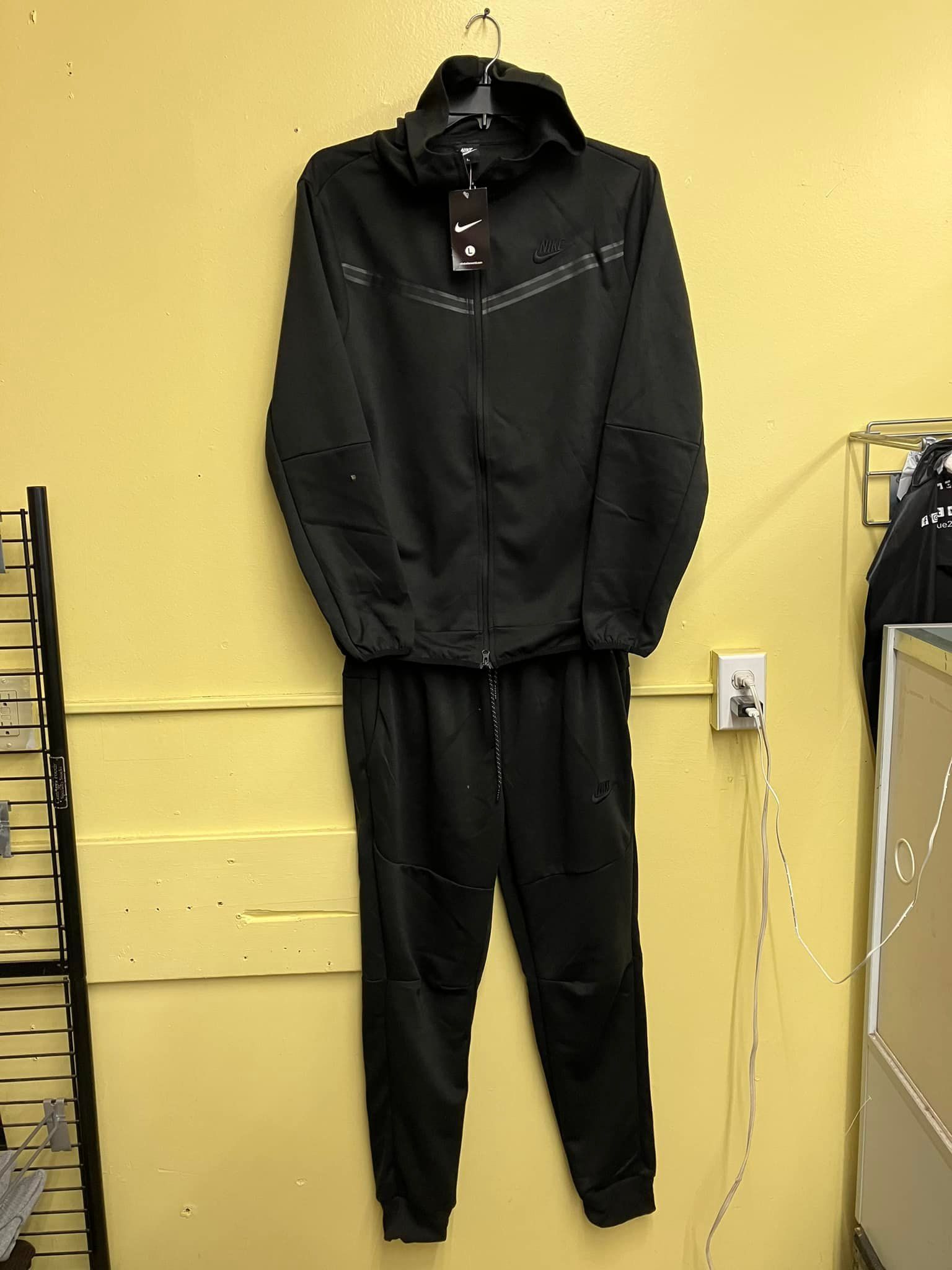 A black zip-up hoodie and matching joggers on a hanger against a yellow wall.