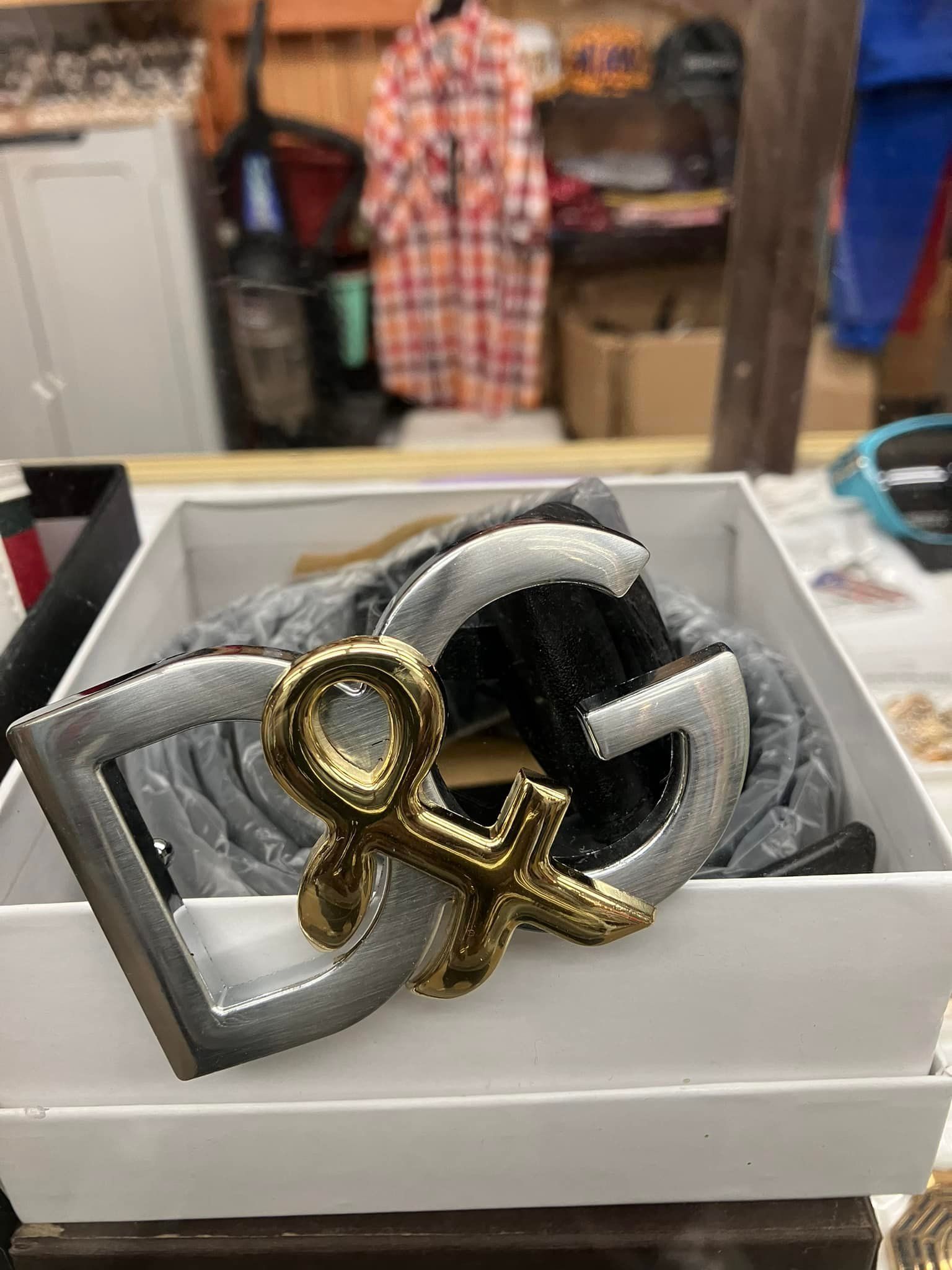 A Dolce & Gabbana belt featuring a large, silver DG logo buckle with an ornate gold detail, displayed in a white box.