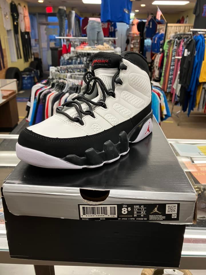 A white and black Air Jordan 9 sneaker sitting on its retail box in a clothing store.