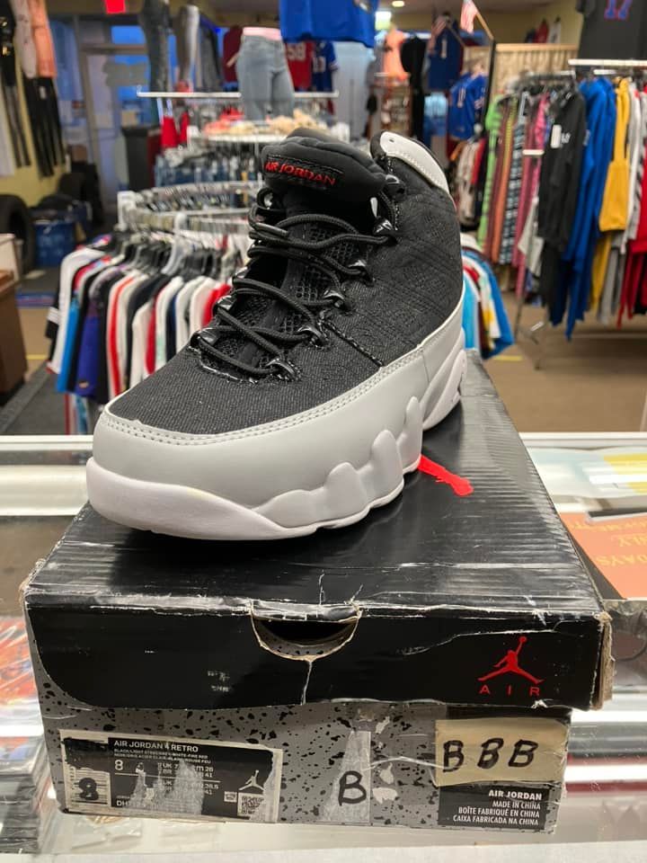 A grey and black Air Jordan 9 sneaker rests on its worn, branded shoebox inside a retail store.