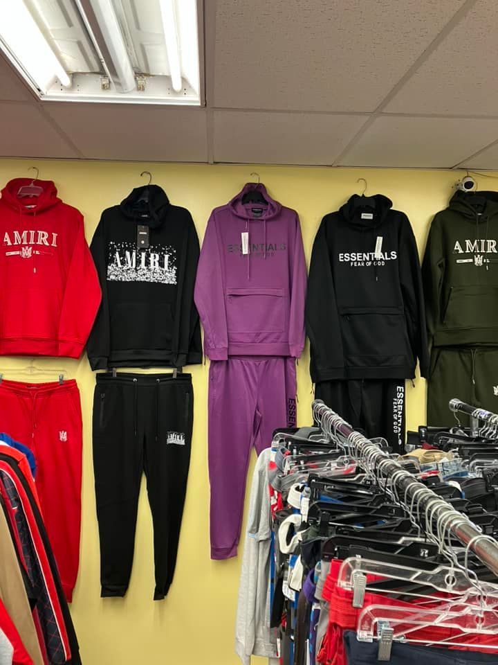 Several tracksuits, including red, black, purple, and olive-green sets, hang on a wall display above a clothing rack.