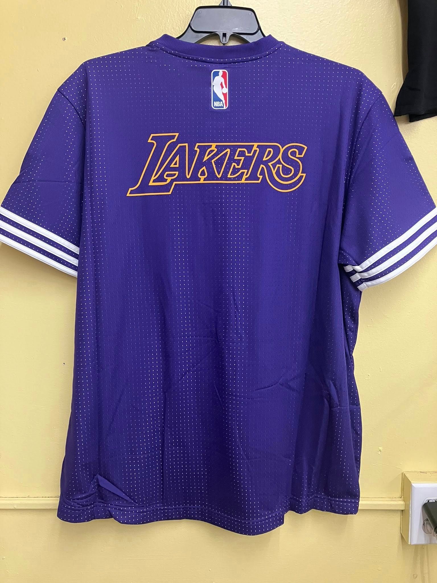 A purple Los Angeles Lakers t-shirt with gold lettering, white sleeve stripes, and a small NBA logo on a hanger.