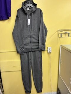 A gray, zip-up hooded sweatshirt and matching sweatpants set hangs against a plain yellow wall.