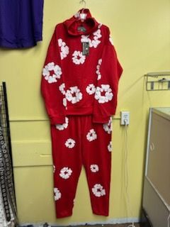A red matching sweatshirt and sweatpants set featuring a white floral pattern, hanging on a hanger against a yellow wall.