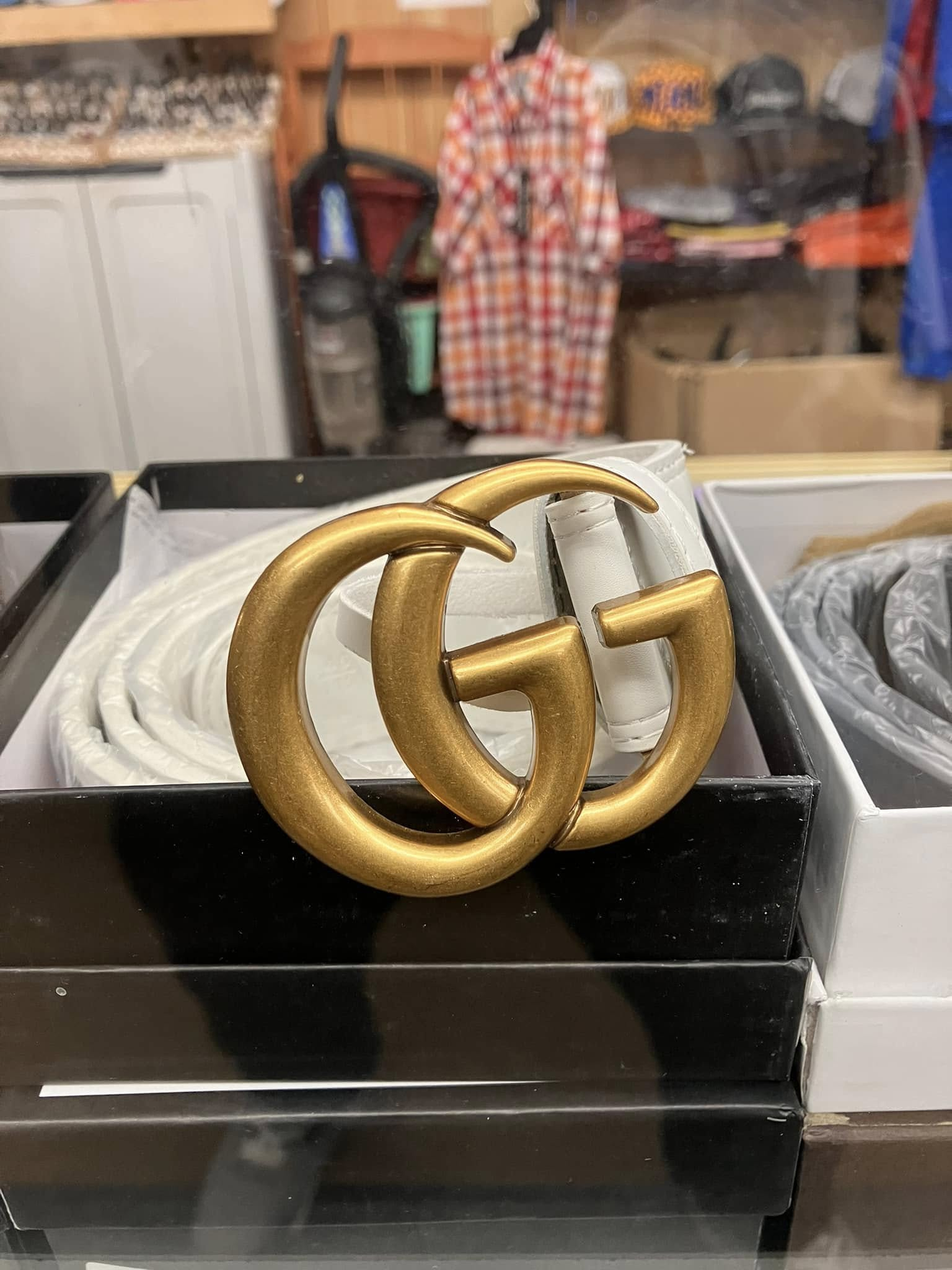 A white leather Gucci belt with a textured gold-tone GG logo buckle inside a black box.